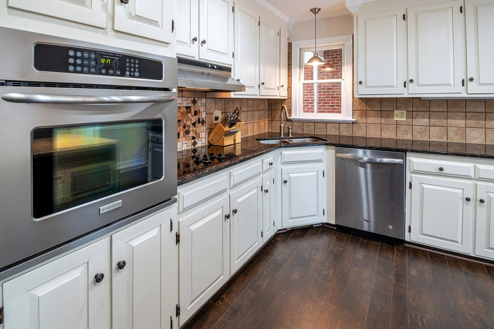 A kitchen with white cabinets and a dark wood floor.